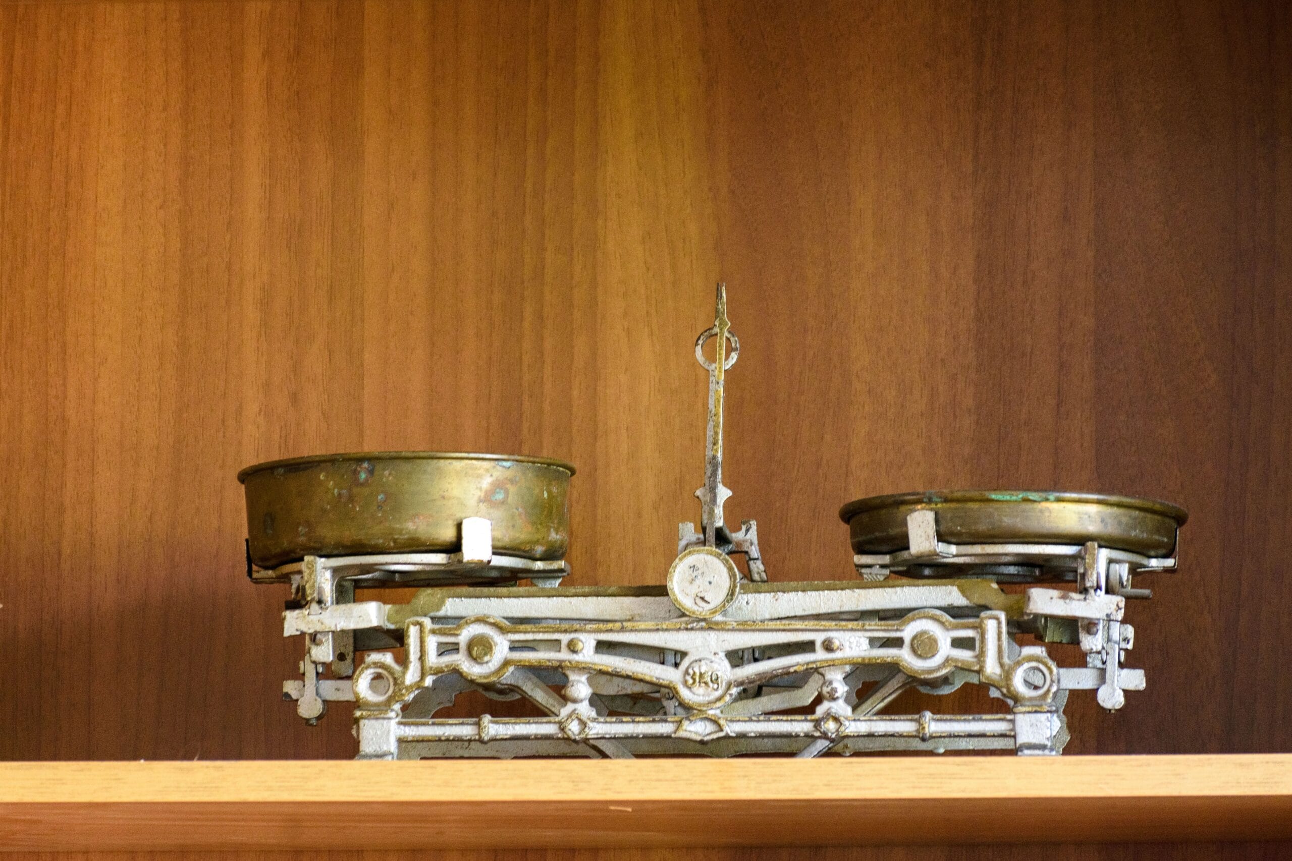 Retro brass kitchen balance scale with symmetry displayed on wooden shelf.